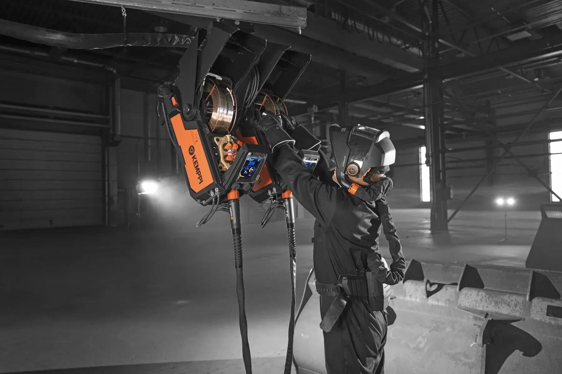 A welder using an X5 wire feeder hung from a boom in a large hall