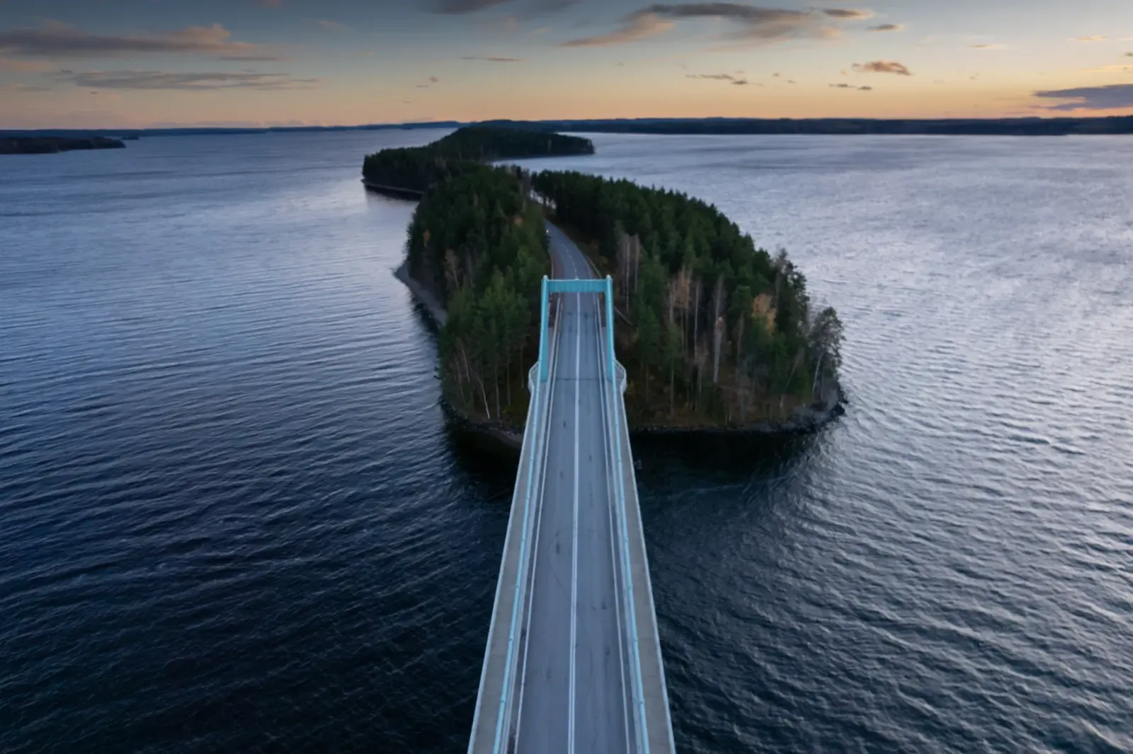 Aerial view of a long bridge crossing water to a forested island at dusk